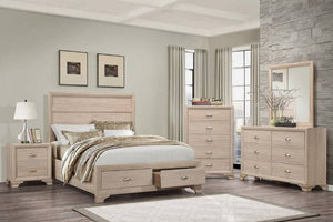 Beige bedroom set with bed, nightstand, dresser with mirror and a chest in a room with gray walls and a stone wall.