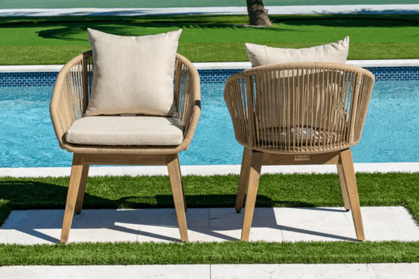 Two wicker chairs with beige cushions by a poolside.