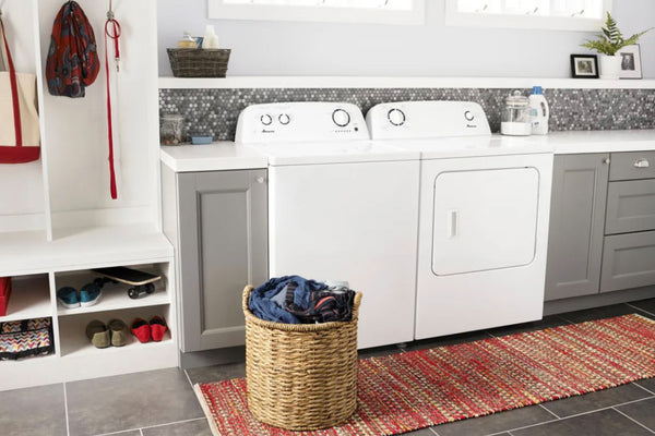 Cuarto de lavado con lavadora y secadora blancas, cesto para ropa y estantes.