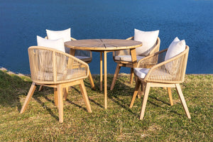 Outdoor furniture set with round table and chairs on a grassy area by a body of water.