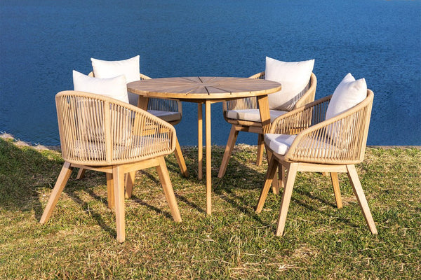 Outdoor furniture set with round table and chairs on a grassy area by a body of water.