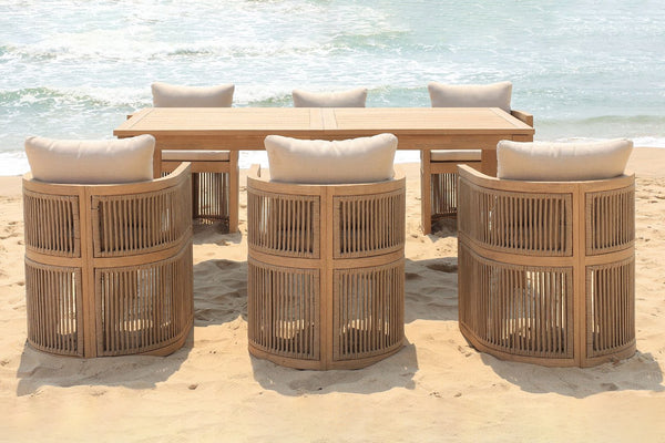 Beige wooden dining table with six matching beige and woven chairs with white cushions on a beach background