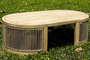 Round wooden outdoor coffee table with wicker sides and a small opening in the middle on grassy background.