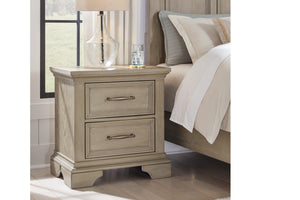 Rustic, wooden nightstand with two light bronze drawers to the left of a bed in a bedroom setting.