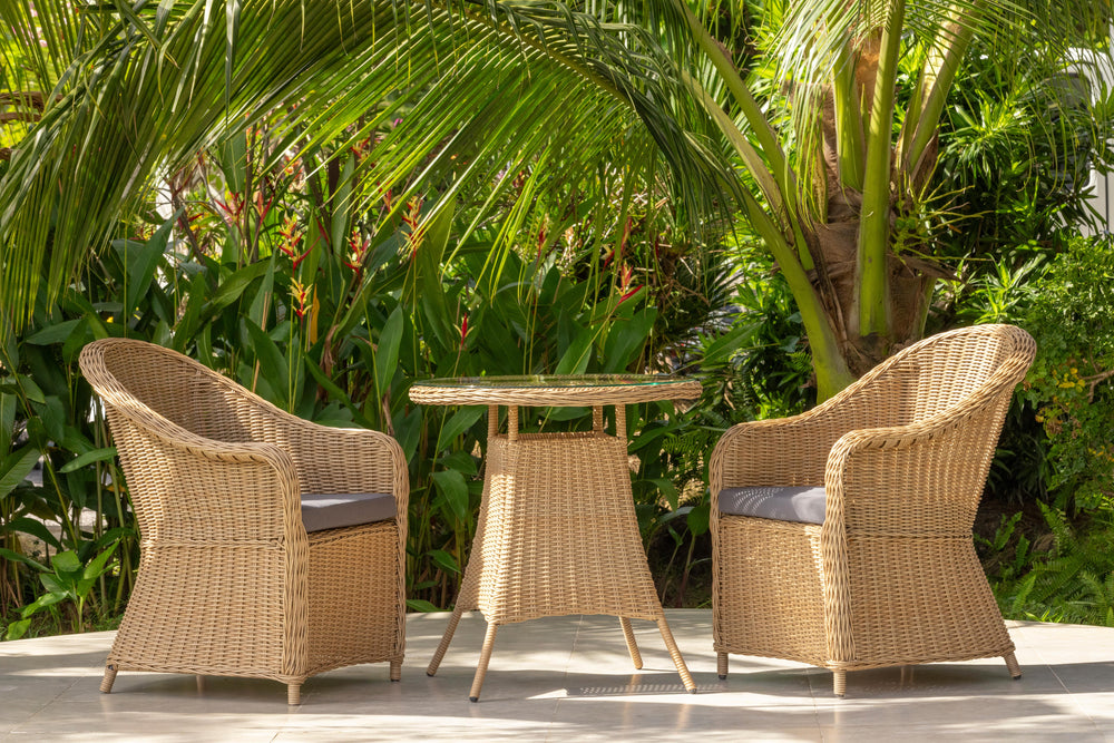 Wicker chairs and table set on a patio with lush greenery in the background
