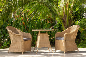 Wicker chairs and table set on a patio with lush greenery in the background