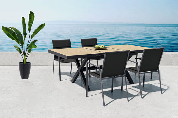 Outdoor beige table with black sides and with four armchairs by the ocean.