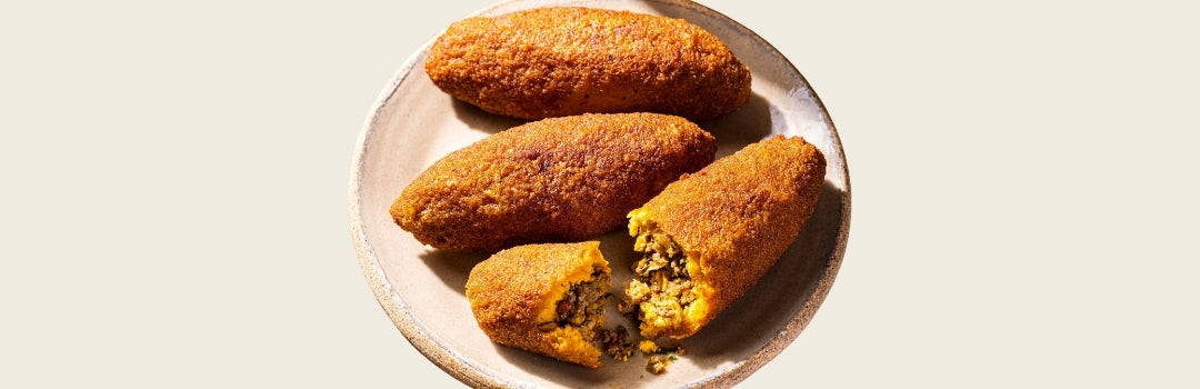 Tres alcapurrías marrones en un plato, todo sobre un fondo crema. 