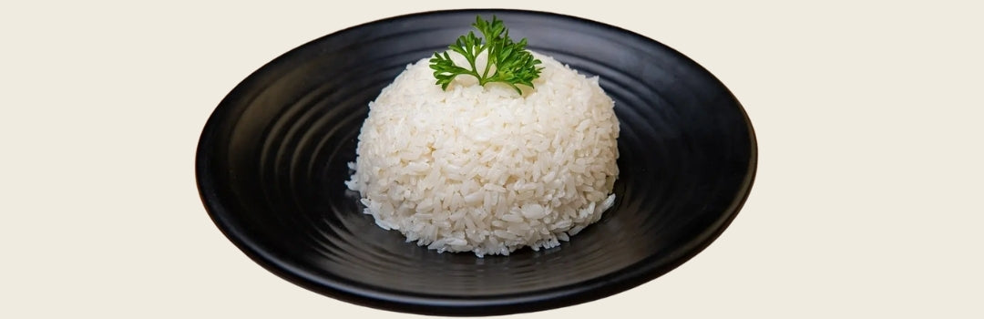 Arroz blanco servido en un plato negro con cilantro encima, todo sobre un fondo crema.
