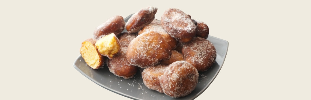 Buñuelos de calabaza con azúcar encima servido en un plato gris, todo sobre un fondo crema.