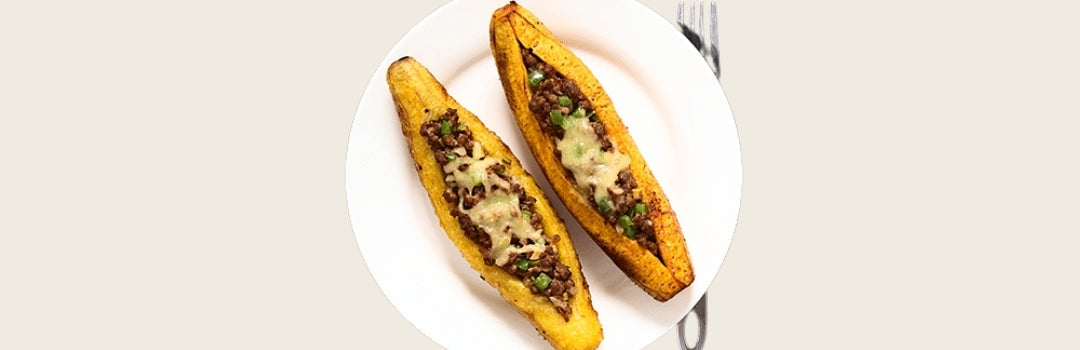 Dos canoas de plátanos maduros servido en un plato blanco con tenedor sobre un fondo crema.
