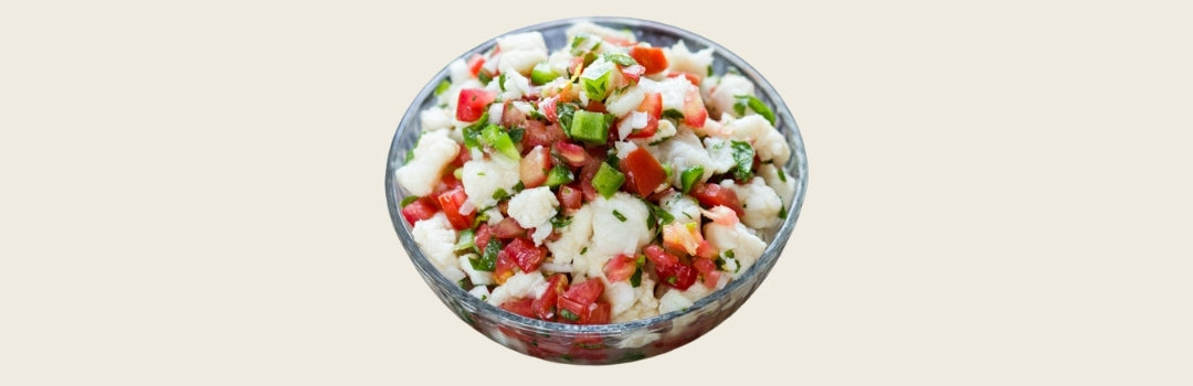 Ceviche en un plato transparente con vegetales sobre un fondo blanco.