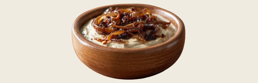 Dip de cebolla caramelizada en un plato de madera marrón sobre un fondo crema.