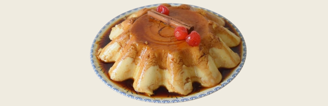 Flan de calabaza con una rama de canela encima y tres cherries servido en un plato decorativo, todo sobre un fondo crema.