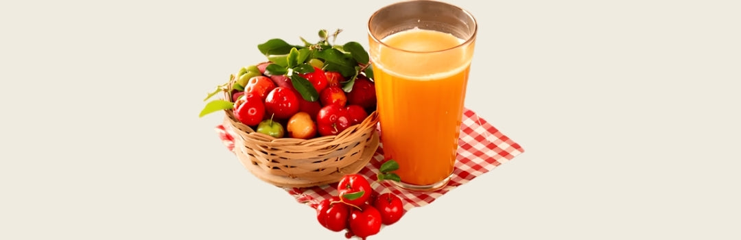 Jugo de acerola en un vaso de vidrio encima de una manta cuadrada roja, una canasta al lado izquierdo con acerolas, todo sobre un fondo crema.