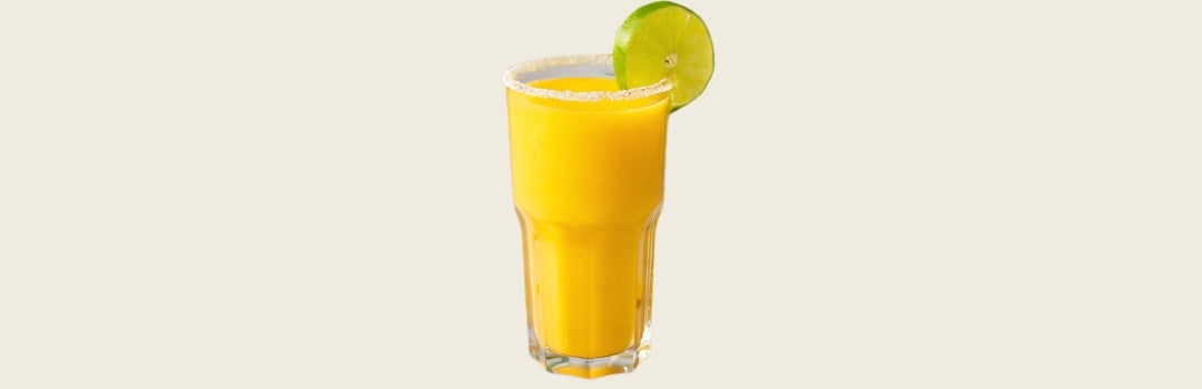 Limonada de mango en un vaso de vidrio con una rodaja de limón en el borde, todo sobre un fondo crema. 