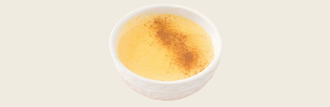 Un pudín de maíz con canela encima servido en un plato blanco sobre un fondo crema.