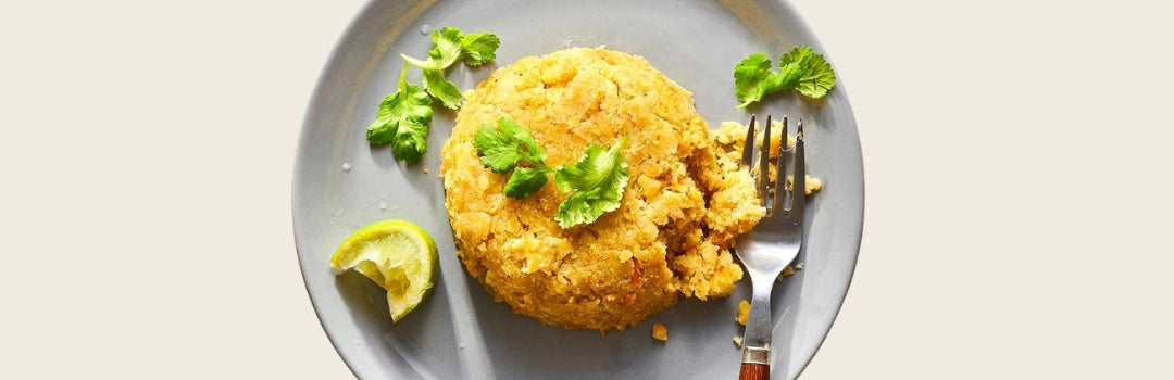 Mofongo servido en un plato con cilantro, una rodaja de limón y un tenedor, todo sobre un fondo blanco.