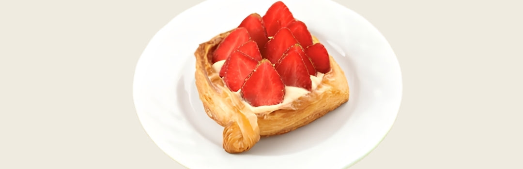 Pastel de crema y fresas encima servido en un plato blanco, todo sobre un fondo crema.