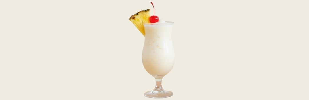 Piña colada con un pedazo de piña en el borde de una copa y un cherry, todo sobre un fondo crema.