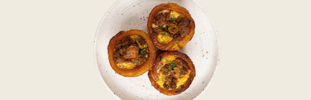 Tres piononos de plátano maduro con carne adentro servido en un plato blanco sobre un fondo crema.