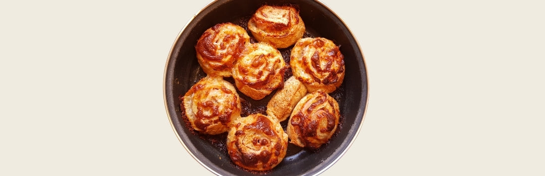 Siete rollos de jamón y queso servido en un plato negro sobre un fondo crema.