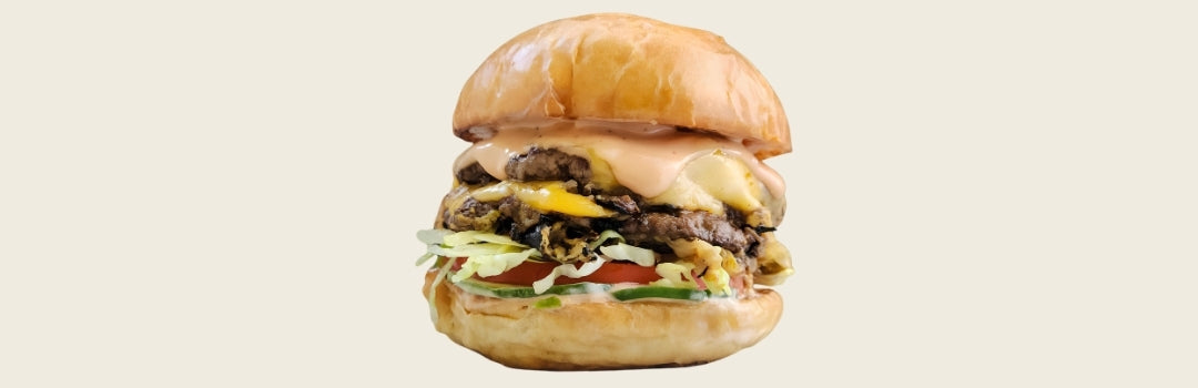 Hamburguesa con carne, lechuga, tomate y salsa sobre un fondo crema. 