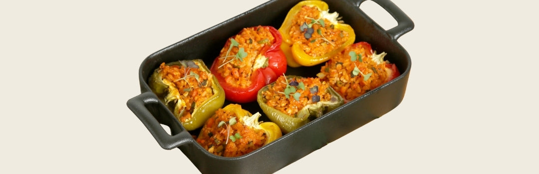 Seis pimientos rellenos de carne molida, arroz amarillo y cilantro servido en un envase negro sobre un fondo crema.