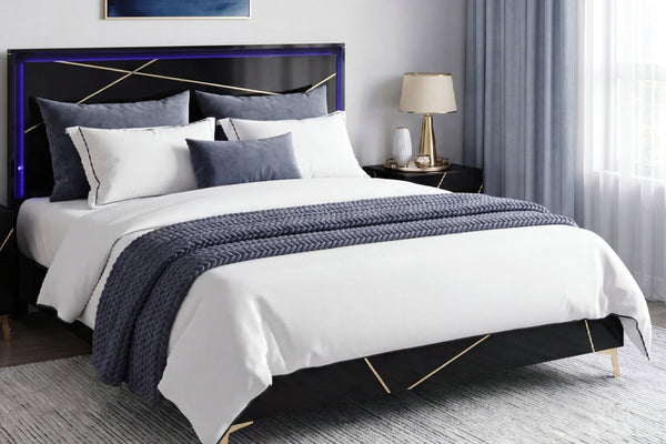 Una cama moderna con estructura negra y detalles geométricos dorados, vestida con ropa de cama blanca y una manta decorativa azul marino texturizada, ubicada en un dormitorio decorado con estilo.