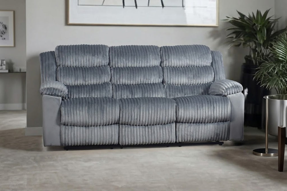 Un sofá reclinable de tres plazas tapizado en tela acanalada gris con textura, en un salón moderno con una planta y una mesa auxiliar.
