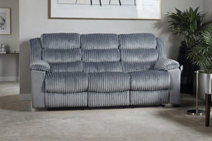 Un sofá reclinable de tres plazas tapizado en tela acanalada gris con textura, en un salón moderno con una planta y una mesa auxiliar.