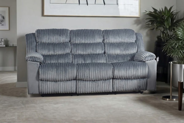 Un sofá reclinable de tres plazas tapizado en tela acanalada gris con textura, en un salón moderno con una planta y una mesa auxiliar.