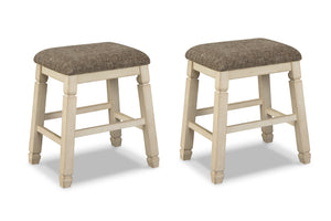 Dos taburetes de bar a juego, con patas de madera pintadas en color crema claro y asientos cuadrados tapizados en tela texturizada color topo, mostrados sobre un fondo blanco.