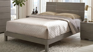 Una moderna estructura de cama de plataforma de madera gris con un cabecero rectangular alto, decorada con ropa de cama y almohadas de color beige en una habitación luminosa.