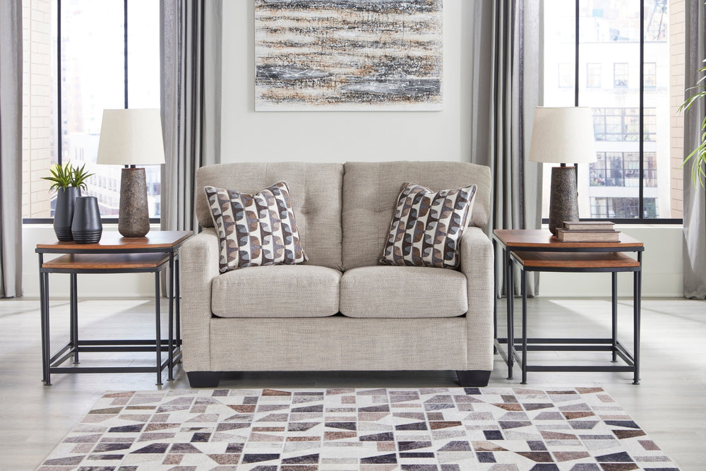 Loveseat de color beige con cojines decorativos sobre un fondo blanco. 