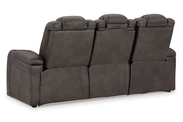 Vista lateral de butaca reclinable eléctrico de color marrón oscuro, una cabecera inclinada hacia atrás con luces LED, un reposapiés extendido, y luces LED azules debajo del reclinable, en un fondo blanco. 