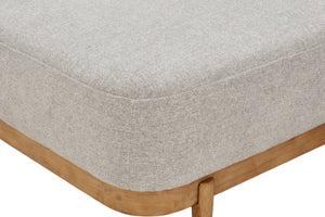 Primer plano de la esquina de un mueble tapizado en gris claro, con estructura y pata de madera natural visibles sobre un fondo blanco.