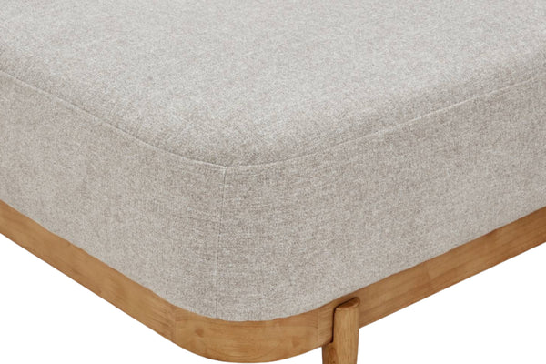 Primer plano de la esquina de un mueble tapizado en gris claro, con estructura y pata de madera natural visibles sobre un fondo blanco.