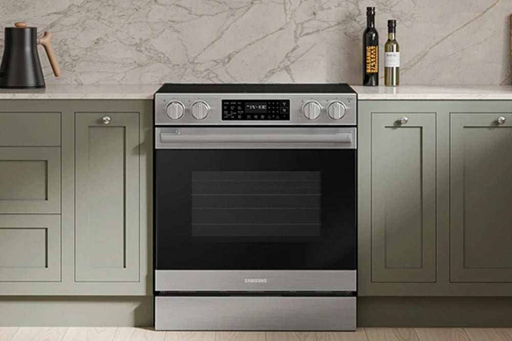 Una estufa eléctrica Samsung blanca con cubierta y puerta de horno, ubicada entre gabinetes de cocina verde salvia contra un counter de mármol.