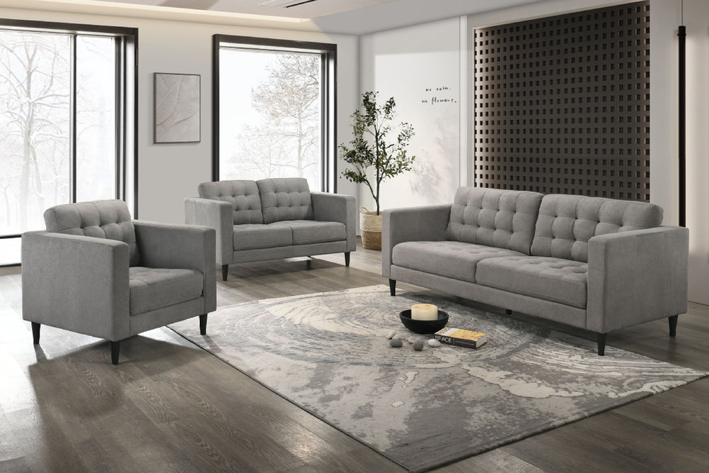 Conjunto de sofá y loveseat gris en una sala de estar moderna con grandes ventanales y elementos decorativos.