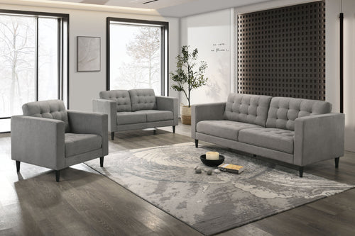 Conjunto de sofá y loveseat gris en una sala de estar moderna con grandes ventanales y elementos decorativos.