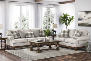Juego de sala tradicional con sofá y loveseat en color beige claro, cojines decorativos a rayas y bases de madera oscura, acompañado de una mesa de centro de madera tallada sobre una alfombra neutra en una sala luminosa con grandes ventanas.