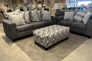 Sofá seccional gris con otomana estampada en un entorno de exposición.