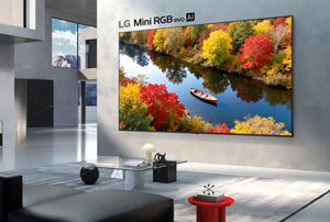 Televisor LG Mini RGB evo AI montado en la pared de una sala moderna, mostrando un paisaje otoñal con árboles coloridos, un río y un bote.