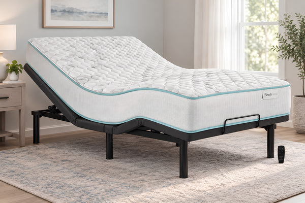 Una base de cama eléctrica ajustable con un mattress acolchado blanco, presentada en un dormitorio luminoso y moderno con una alfombra gris, una mesita de noche y una ventana.