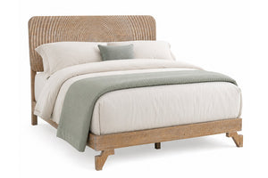 Una cama moderna tipo plataforma con estructura de madera natural clara y cabecero curvo de ratán tejido, decorada con ropa de cama blanca y una manta y almohada de color verde salvia sobre un fondo blanco.
