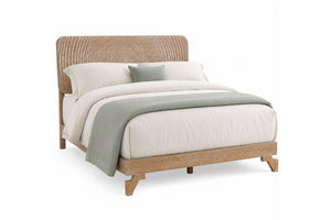 Una cama moderna tipo plataforma con estructura de madera natural clara y cabecero curvo de ratán tejido, decorada con ropa de cama blanca y una manta y almohada de color verde salvia sobre un fondo blanco.