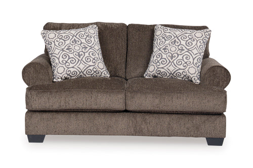 Loveseat de color marrón con cojines decorativos sobre un fondo blanco. 