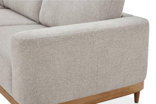 Primer plano del reposabrazos de un sofá tapizado en tela texturizada de color beige claro, con pata de madera marrón claro sobre un fondo blanco liso.