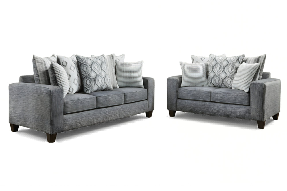 Juego de sala moderno compuesto por sofá y loveseat tapizados en tela gris, con cojines decorativos en patrones geométricos y rayas en tonos gris y blanco, sobre fondo blanco.